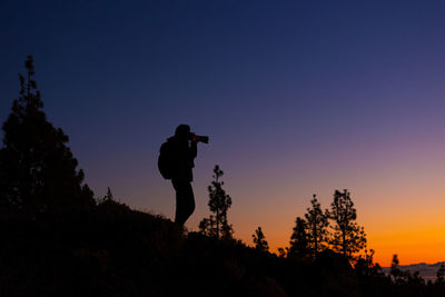 Rear view of man standing on mountain against sky during sunset