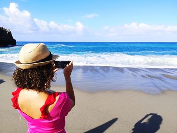 Rear view of woman on beach by sea against sky