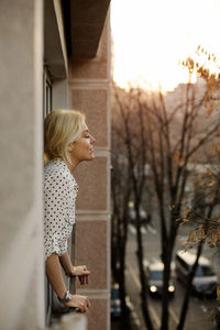 Side view of relaxed woman standing at house window