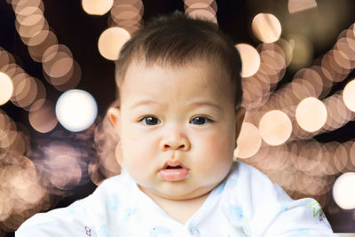 Close-up portrait of cute baby boy against illuminated lights