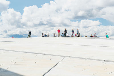 People at oslo opera house against cloudy sky