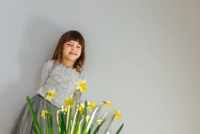 Smiling girl in white top and grey skirt standing behind daffodil flowers