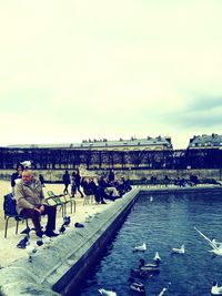 Rear view of people sitting on bridge over river against sky