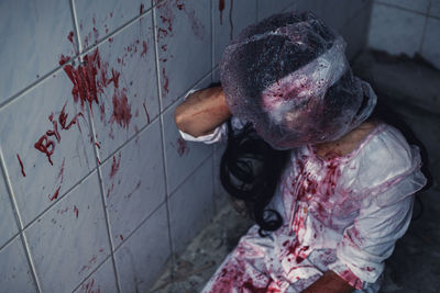 High angle view of young woman with plastic on head kneeling by wall