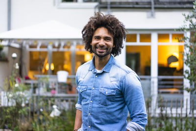 Happy man with afro hairstyle standing in front of house