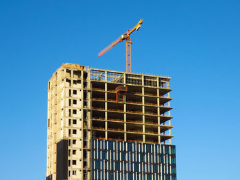 Low angle view of building under construction against clear blue sky