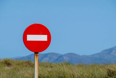 Road sign on field against clear blue sky