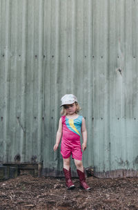 A young girl stands near a barn wearing a leotard and cowgirl boots.