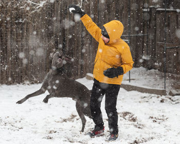 Full length of teenager boy playing with dog during winter