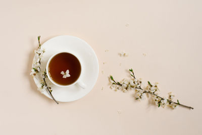 White porcelain cup with black tea and marshmallows. branches of a blossoming apple tree lie