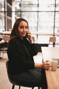 Young woman using phone while sitting on table