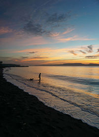 Silhouette people on beach against sky during sunset