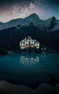 House by lake against mountains during winter