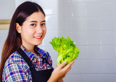 Portrait of young woman holding leafy vegetable at home
