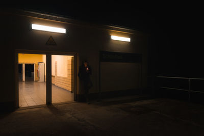 Man using smart phone in dark outside illuminated building