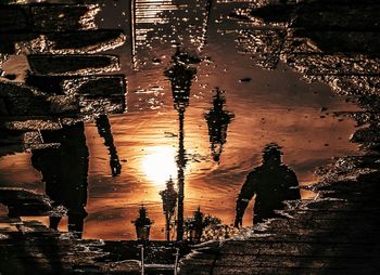 Reflection of silhouette people in water at sunset