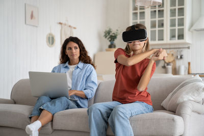 Teen girl child in virtual reality glasses playing games while her mother working remotely at home