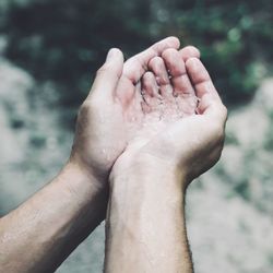 High angle cropped hands holding water over river