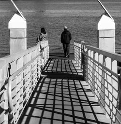 Rear view of people walking on railing by sea