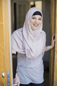 Portrait of smiling young woman standing by open door