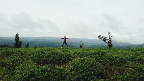 Mid distance view of man with arms outstretched standing on field against sky