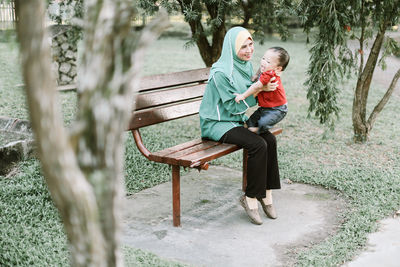 Mother playing with son while sitting on bench at park