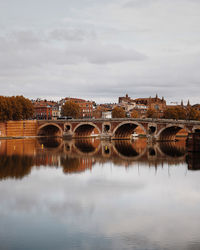 Bridge over river by buildings against sky