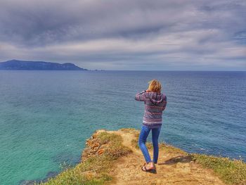 Rear view of woman standing by sea against sky