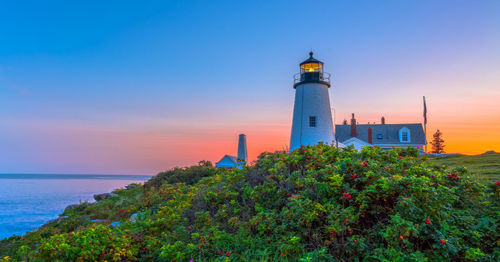 Lighthouse amidst sea and buildings against sky