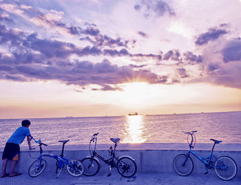 Bicycles on railing by sea against sky during sunset