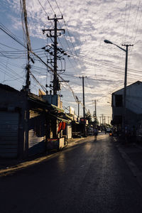 Road by electricity pylon in city against sky