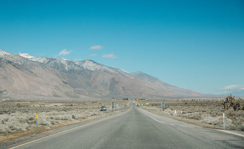 Empty road by mountain against blue sky