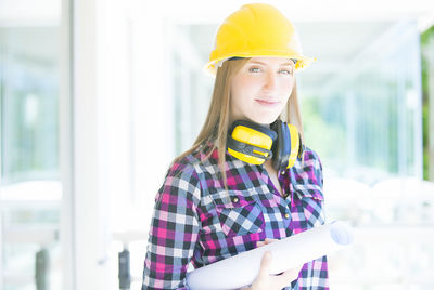 Portrait of confident female engineer with blueprint wearing work helmet