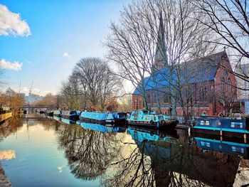 Bare trees by river against sky