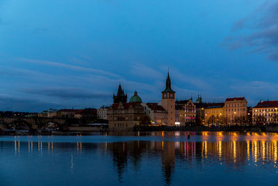 Illuminated buildings by river against sky at dusk