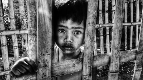 Close-up portrait of homeless boy seen through bamboo fence