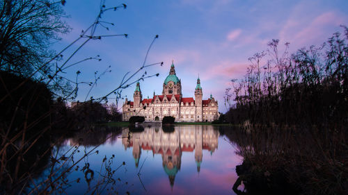 New town hall by lake against cloudy sky during sunset