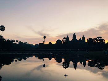 Silhouette temple by lake against sky during sunset