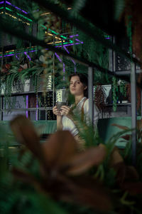 Woman drinking coffee while sitting in greenhouse