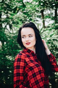 Smiling young woman looking away while standing against plants in forest