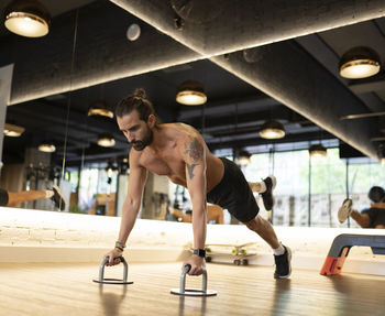 Shirtless adult male athlete doing exercise on push up handles during fitness workout in contemporary gym