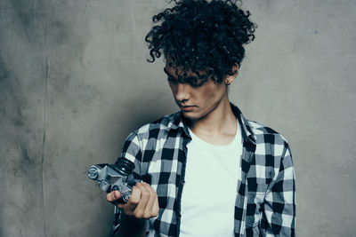 Portrait of young man holding camera against wall