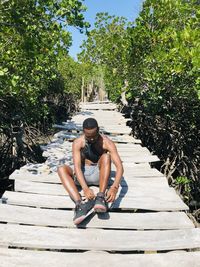 Young woman sitting on wood against trees