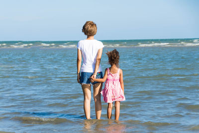 Rear view of siblings standing at beach against clear sky