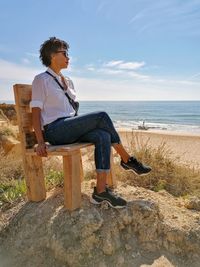 Woman sitting on seat at beach against sky