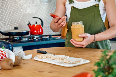 Woman making healthy breakfast or brunch, opening jar with peanut butter for spreading it. 