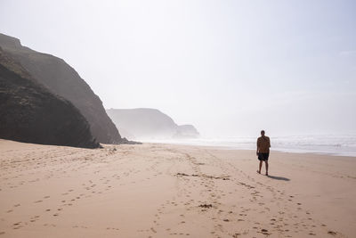 Rear view full length of man walking at beach against clear sky