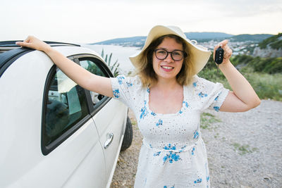 Portrait of smiling young woman standing against car