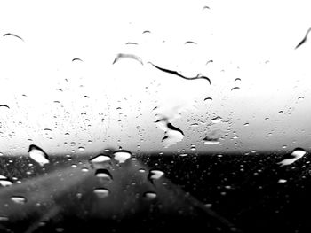 Close-up of water drops on window against sky