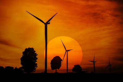 Silhouette wind turbines on field against orange sky